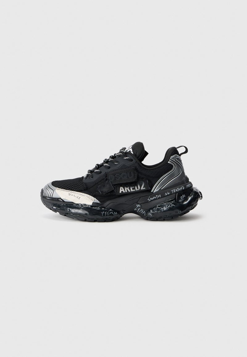 Black athletic shoes with mesh upper, textured accents, and reflective details. Notable black outsole with white handwritten patterns.