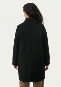 Zwarte wollen coat met een uitgesneden kraag, lange mouwen en een recht model. Bevat minimale details en een schone, geotexteerde oppervlakte.