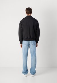 Black bomber jacket with a ribbed hem and cuffs, paired with light blue, loose-fitting jeans and white sneakers, viewed from the back.