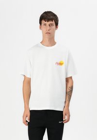 T-shirt bianco in cotone con maniche corte, scollatura rotonda, caratterizzata da una grafica colorata "Holidays" sopra un sole giallo sul petto.