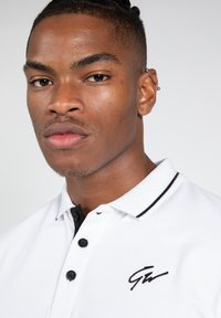 Witte poloshirt met zwarte knopen en een zwarte kraag. Bevat geborduurd logo aan de linkerkant. Gladde stoftextuur.