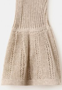 Tela de punto beige que muestra una sección superior acanalada y patrones de encaje calado en la parte inferior acampanada.