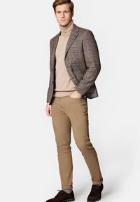 Marynarka w kratę w brązowo-niebieskim kolorze, beżowy golf, brązowe spodnie i ciemne buty. Teksturowana tkanina, dopasowany krój oraz subtelne detale wzoru.