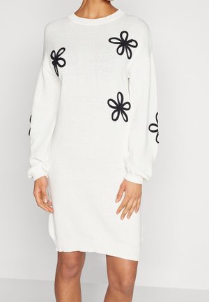 Abito in maglia bianco con motivi floreali neri, scollo tondo e maniche lunghe. Presenta polsini a coste e una vestibilità ampia.