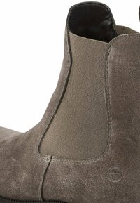 Bottine Chelsea en daim gris avec des panneaux élastiques sur les côtés, un bout arrondi et une finition texturée. Détail de logo notable sur le talon.