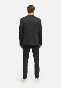Mørk grå dress med en tilpasset passform, med en enkel vent og matchende bukser. Båret med hvite sneakers for kontrast.
