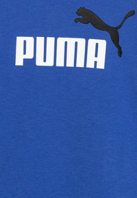 T-shirt in cotone blu con un grande logo bianco "PUMA" e una silhouette nera di un puma in salto sopra il testo. Texture liscia.