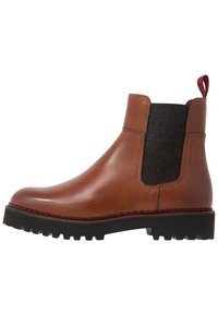 Botte Chelsea en cuir brun avec panneau latéral élastique, tissu texturé, tirant rouge et semelle extérieure noire robuste avec un motif de bande de roulement.