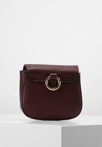 Sac à main en cuir bordeaux à la forme arrondie, doté d'une fermeture à rabat et de quincaillerie en or. Texture lisse avec des coutures contrastées.