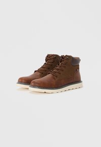 Botas de cuero marrón con acentos de ante, puntera redonda y diseño de cordones. Cuenta con una suela de goma color crema y detalles de costura en contraste.