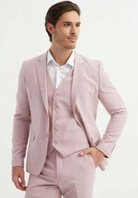 Costume trois pièces rose clair composé d'un blazer ajusté, d'un gilet avec boutons et d'un pantalon assorti ; tissu lisse avec un léger éclat.