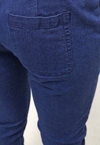 Gros plan sur la poche arrière et la partie supérieure de la jambe d'un jean en denim bleu foncé.