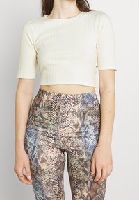 Krémový žebrovaný cropped top s krátkými rukávy, kombinovaný s legínami s vysokým pasem a vícbarevným vzorem hadí kůže.