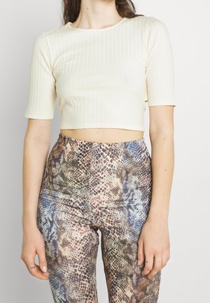 Top corto de canalé crema con mangas cortas, combinado con leggings de tiro alto que presentan un patrón de piel de serpiente multicolor.