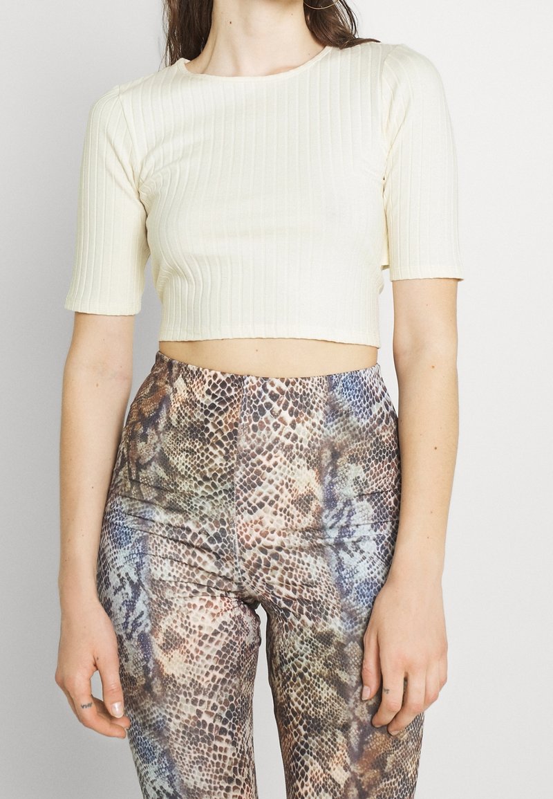 Krémový žebrovaný cropped top s krátkými rukávy, kombinovaný s legínami s vysokým pasem a vícbarevným vzorem hadí kůže.