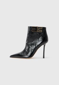Black leather ankle boot with a pointed toe, high heel, and gold logo accents on the ankle. Smooth texture with a glossy finish.