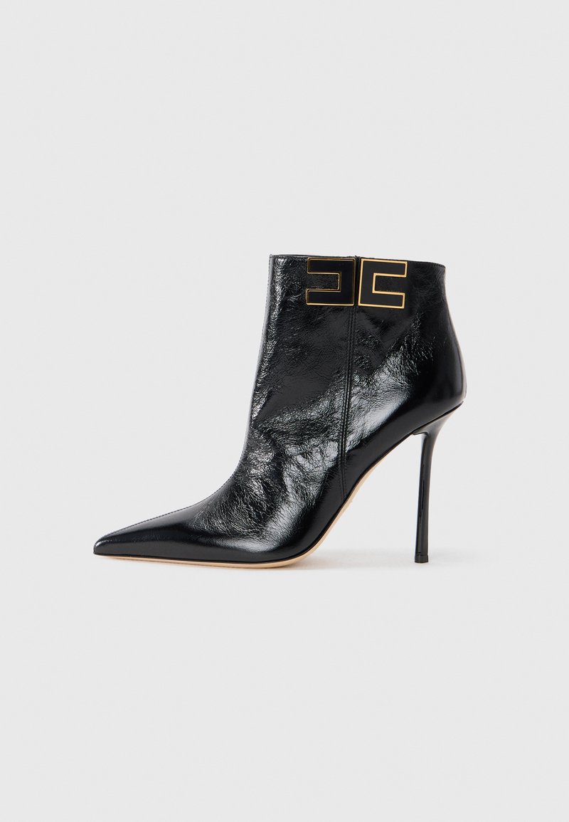 Black leather ankle boot with a pointed toe, high heel, and gold logo accents on the ankle. Smooth texture with a glossy finish.
