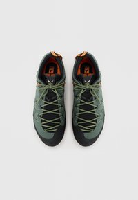 Groene en zwarte wandelschoenen hebben een bovenwerk van gaas, een gekarteld rubberen zool en patroon veters voor een veilige pasvorm. Oranje accenten op de hiel.