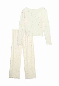 Tvådelat pyjamasset i krämfärg med små rosa hjärtan. Topp med lång ärm och rundad halslinning; löst sittande byxor med elastisk midja.