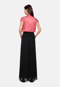 Rosa Satinbluse mit kurzen Spitzenärmeln, kombiniert mit schwarzen, weit geschnittenen Hosen mit hoher Taille und durchsichtigen Stoffakzenten.