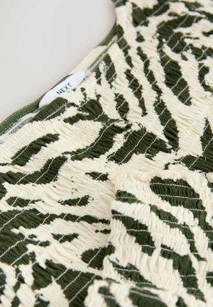 Zelená a krémová vzorovaná látka s nariasenou textúrou, zdobená listovým motívom. Štítok s nápisom "NEXT" sa nachádza blízko hornej hrany.