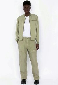 Veste bomber vert clair et pantalon cargo assorti. La veste présente une fermeture éclair sur le devant et un logo brodé. Le tissu a une texture lisse.
