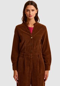 Brązowy strój z cordurowej tkaniny z wysokim kołnierzem, długimi rękawami i zapięciem na guziki, z teksturowaną powierzchnią i paskiem w talii.