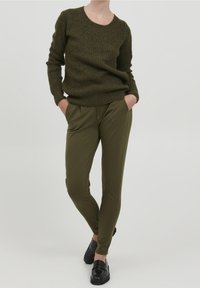 Olijfgroene gebreide trui met een ronde halslijn, gecombineerd met olijfgroene tapered pants. Zwarte instappers, gladde oppervlakte. Eenvoudig ontwerp.