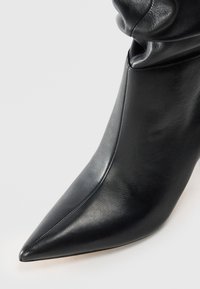 Black leather ankle boot with a pointed toe and smooth texture. Features a fitted design and subtle stitching detail along the seams.