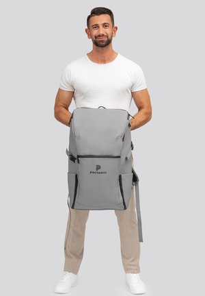 Zaino grigio con un design elegante, multiple tasche, spallacci regolabili e un logo sul davanti. Texture liscia e forma funzionale.