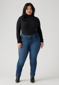 Black long-sleeve top paired with mid-rise blue denim jeans. Jeans feature a classic five-pocket design and a slim fit, complemented by black ankle boots.