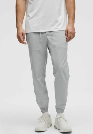 Világosszürke melegítőnadrág, elasztikus szegélyekkel és zsinóros derékkal, két oldalsó zsebből és sima, matt felületből áll.