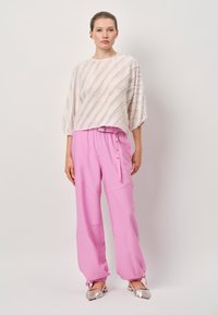 Helle rosa, lockere Hose mit Kordelzug und Druckknopfdetails, kombiniert mit einer strukturierten, cremefarbenen Bluse mit horizontalen Streifen.