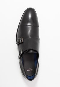 Scarpa in pelle nera con punta affusolata, caratterizzata da due fibbie argentate e una fodera interna blu. Texture liscia e design elegante.