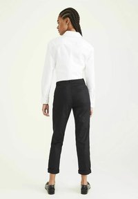 White long-sleeve shirt with a standard collar paired with black rolled-up trousers. Smooth fabric with minimalistic design and no visible patterns.