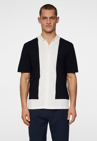 Koszulka polo z krótkim rękawem w dwukolorowym wzorze w granatowym i białym kolorze, z klasycznym kołnierzykiem i zapięciem na guziki, wykonana z gładkiego materiału.