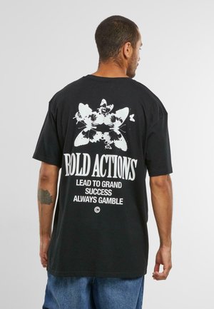 Sort bomulds t-shirt med et stort hvidt sommerfugl grafik og fed tekst på ryggen. Korte ærmer og afslappet pasform.