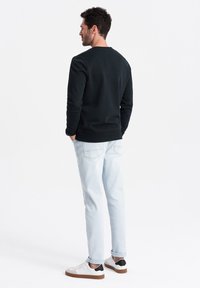 Sudadera negra, cuello redondo, de mangas largas. Vaqueros de un tono azul claro, de corte recto, con puños en los tobillos. Zapatillas blancas con detalles en negro.
