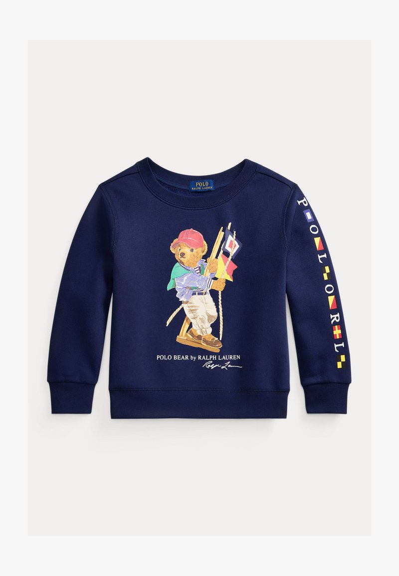 Mornarsko plava majica s dugim rukavima s Polo medvjedom u mornarskoj odjeći koji drži pomorske zastave, tekst "POLO RALPH LAUREN" na rukavu i logotip ispod medvjeda.