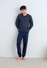 Pull marin à motif quadrillé blanc, à manches longues et avec des poignets côtelés, associé à un pantalon marin assorti, en tissu lisse, au design ajusté.