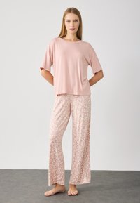 Top rosa chiaro a maniche corte abbinato a pantaloni larghi con una delicata stampa leopardata in tonalità chiare e scure. Tessuto morbido, design casual.