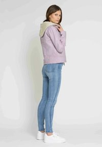 Lavendel læderjakke med en beige hætte, lynlås foran og slim fit, parret med blå skinny jeans og hvide sneakers.