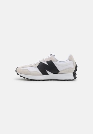 Baskets blanches et beiges avec un logo noir "N" sur le côté, des lacets blancs et une semelle noire texturée, vues de profil.