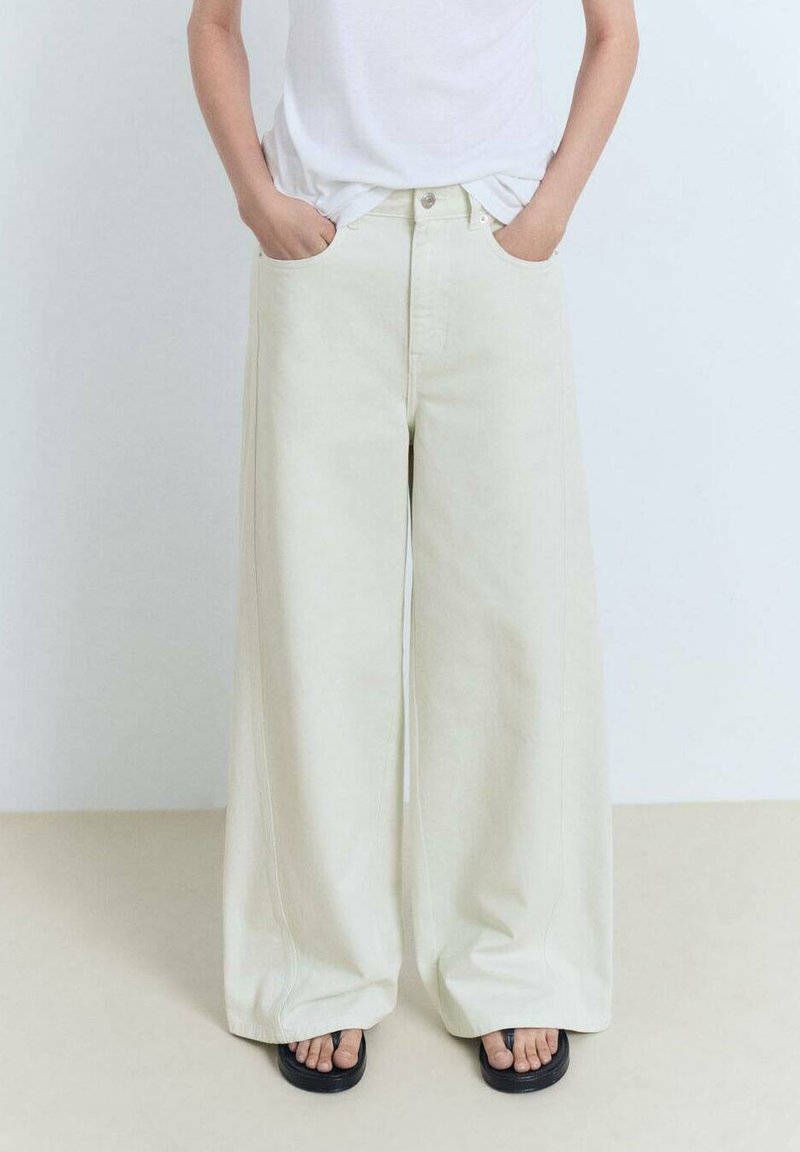 Široke hlače bež barve izdenima, z dvema sprednjima žepoma in minimalističnim dizajnom. Nosi se jih z preprosto belo majico in sandalami.