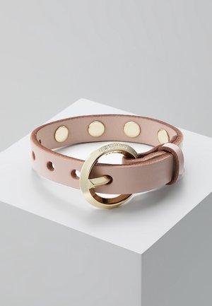 Bracelet en cuir rose clair avec boucle ronde en or et boutons-pression dorés, présenté sur une surface géométrique blanche.
