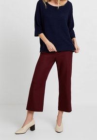 Granatowy, dziany, oversize'owy sweter, bordowe spodnie o kroju cropped oraz beżowe buty na szerokim obcasie. Materiał o wyraźnej fakturze, szerokie rękawy i luźny krój.