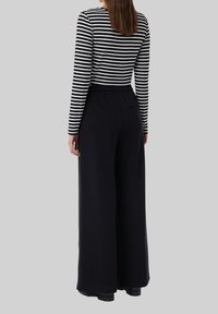 Un pantalon large noir associé à un haut à manches longues rayé, avec une taille élastique et un détail de poche arrière.