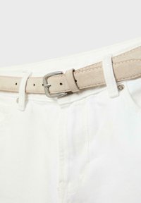 Ceinture en daim beige avec boucle en argent attachée aux passants de ceinture d'un jean blanc en denim.