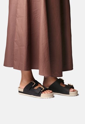 Čierne sandále s dvoma šnurovacími prackami, s textúrovaným vrchným dielom a podrážkou lemovanou jutou. Podrážka je mierne zdvihnutá s vzorom dezénu.