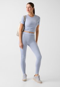 Hellblaues, kurz geschnittenes Sportoberteil und passende Leggings aus dehnbarem Material mit subtiler Textur und figurbetontem Design. Weiße Turnschuhe.